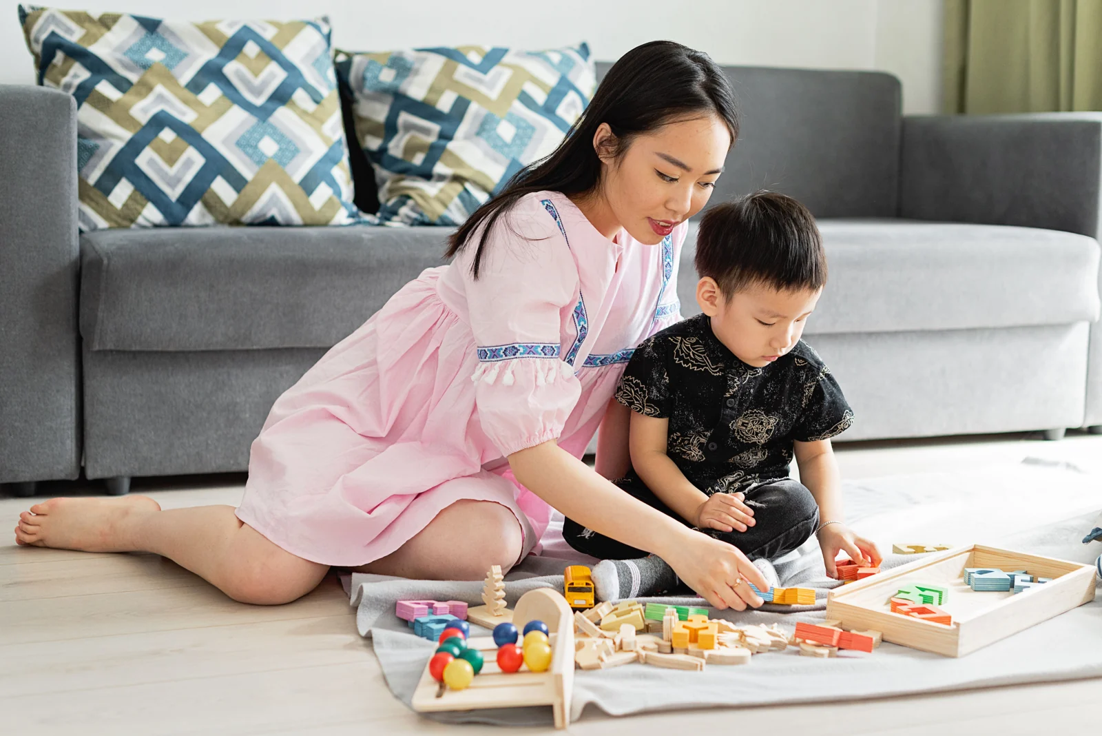 母亲坐在孩子身边，陪伴他尝试木质拼搭玩具